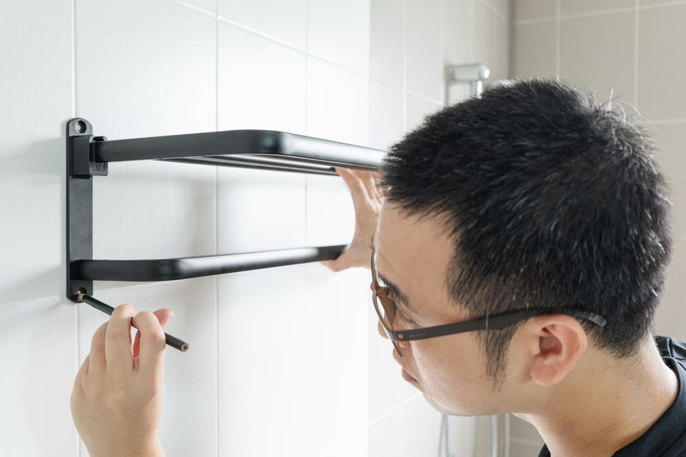 Asian man preparing to install a towel rail on the bathroom wall He put the rack against the wall and used a pencil to mark where to drill.